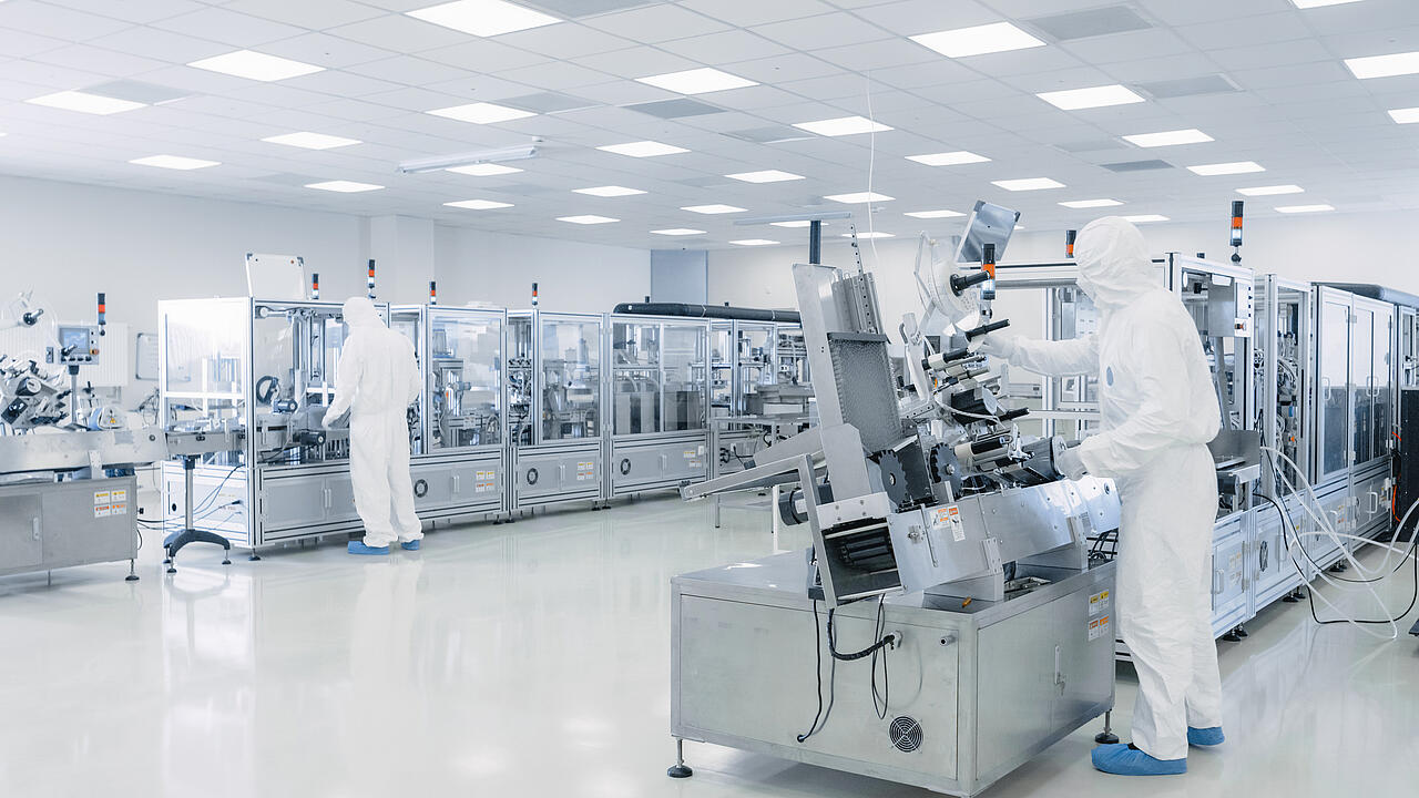 Nave de producción dedicada a la investigación en semiconductores, con científicos equipados con material de protección junto a las máquinas