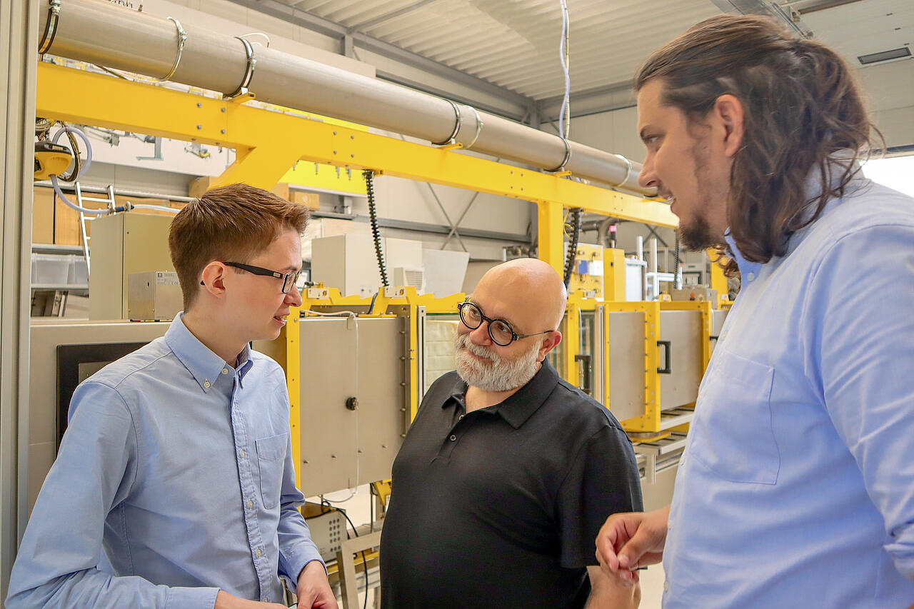 Site de production équipé d'un banc de test, avec trois personnes en train de discuter devant celui-ci